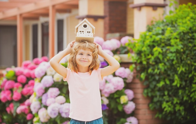 Onroerend goed huisvesting en familie concept Grappige jongen met speelgoed houten huis in de buurt van nieuw huis