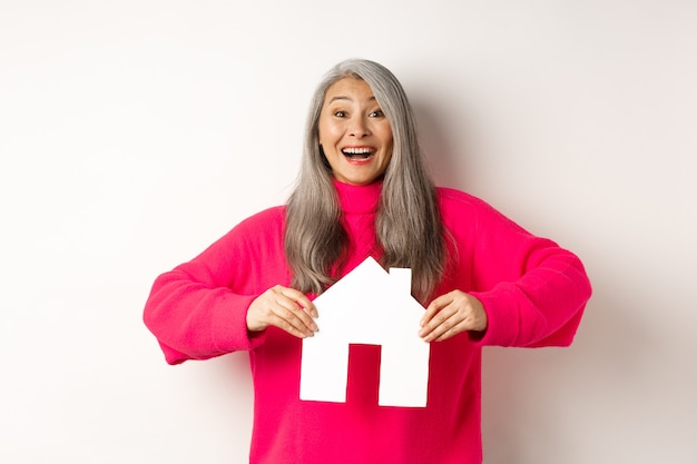 Onroerend goed opgewonden aziatische senior vrouw die op zoek is naar een gelukkig en gelukkig winnend appartement met papieren huis ...