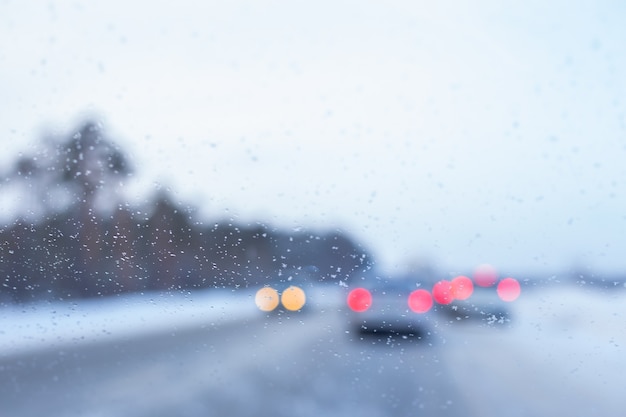 Onscherpe achtergrond van de voorruit van een auto met sneeuwvlokken en auto's op de achtergrond