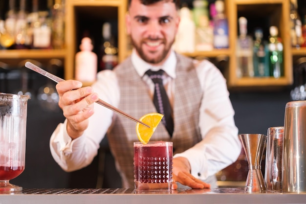 Onscherpe jonge mixoloog die zijn cocktail versiert voor een perfecte presentatie aan de klant focus op de beker Concept Hospitality barman serve