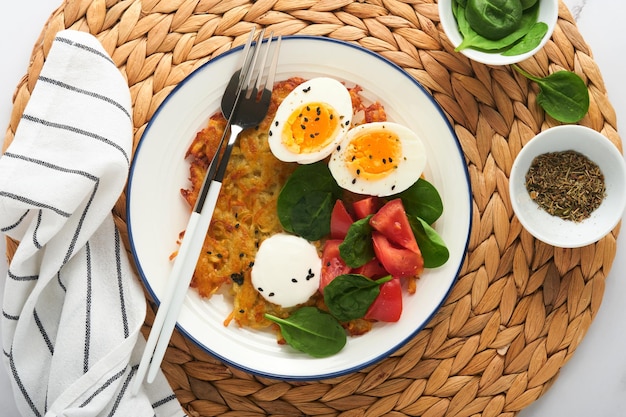 Ontbijt Aardappelen latkes met zure room spinazie salade tomaten en gekookte eieren op lichte marmeren tafel achtergrond Heerlijk eten voor het ontbijt Bovenaanzicht