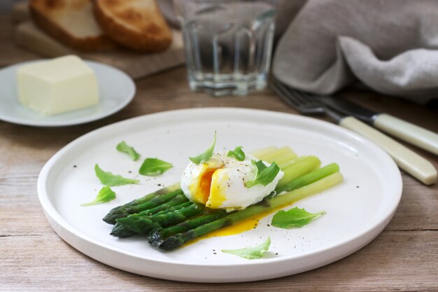 Ontbijt bestaande uit gepocheerd ei en gekookte asperges met boter en sla op een houten oppervlak. Rustieke stijl.