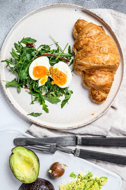 Ontbijt, brunch met avacado, rucola, croissant en ei. grijs oppervlak. bovenaanzicht