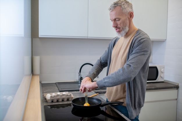 Ontbijt. Een grijsharige man die omelet kookt in de keuken