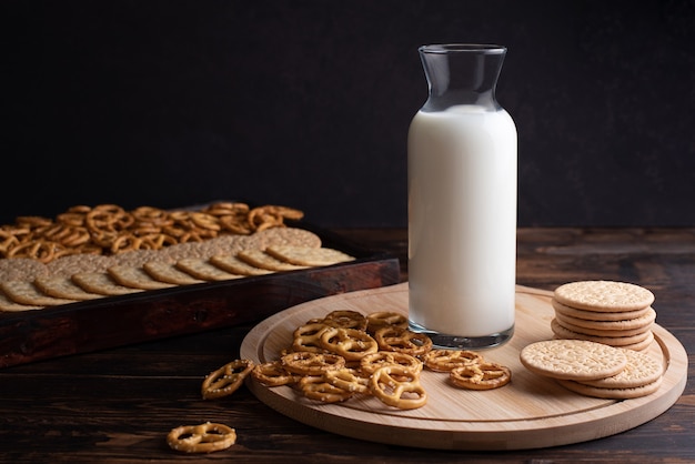 Ontbijt en snack melkfles met koekjes en mini gezouten pretzels op een donkere houten achtergrond.