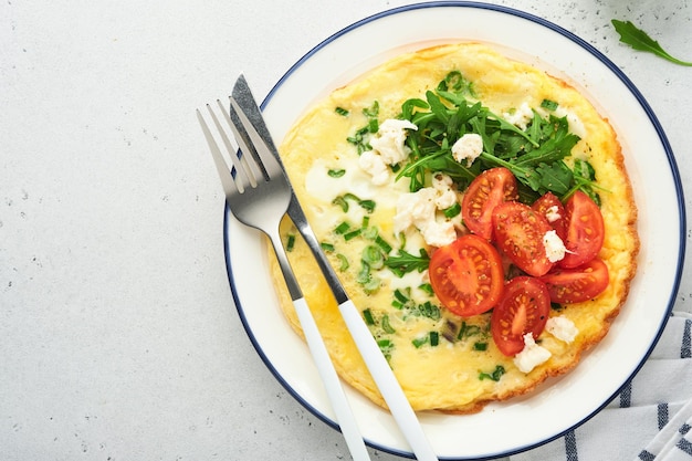 Ontbijt gebakken eieren Rustieke omelet of frittatas met groene uien kaas mozzarella groene rucola en tomaten op lichte stenen achtergrond Gezonde voeding concept Kopieer ruimte Bovenaanzicht Mock up