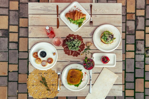 Foto ontbijt geserveerd café tafel met kaas pannenkoeken, sandwich, croissant en drankjes. bovenaanzicht