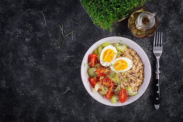 Ontbijt havermoutpap met gekookt ei, cherrytomaatjes, selderij en microgreens. Gezonde evenwichtige voeding. Bovenaanzicht, hierboven, kopieer ruimte