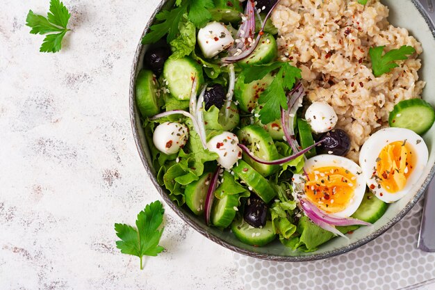 Ontbijt havermoutpap met gekookte eieren komkommer mozzarella kaas en groene kruiden gezond uitgebalanceerd voedsel bovenaanzicht