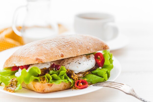 Ontbijt in rustieke stijl op een witte houten ondergrond. ciabatta met gepocheerd ei en graanmosterd bij een warme kop koffie en vers