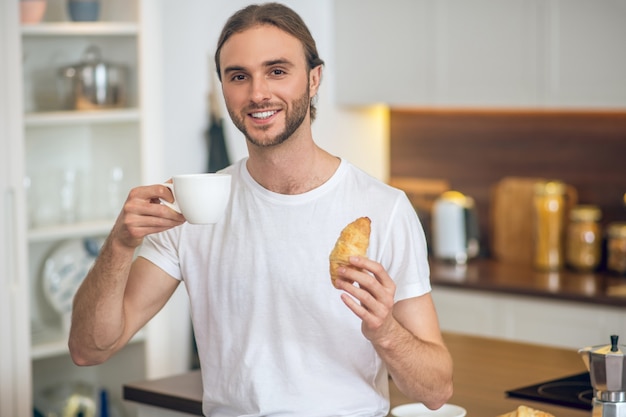 Ontbijt. Jonge man in homewear staande in de keuken met een koffiekopje in de hand