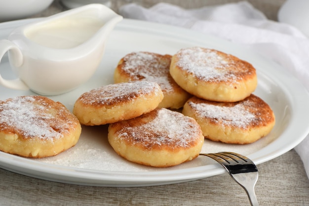 Ontbijt. Kaaspannenkoekjes met zure room bestrooid met poedersuiker op een witte plaat.