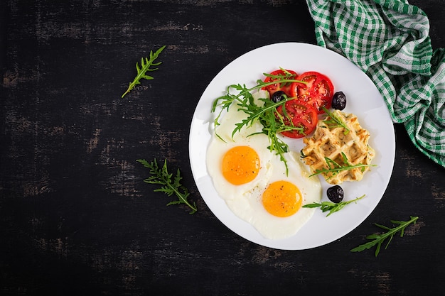 Ontbijt met courgette wafels, gebakken eieren, tomaat, zwarte olijven en rucola op witte achtergrond. Voorgerechten, snack, brunch. Gezond vegetarisch eten. Bovenaanzicht, overhead, kopieerruimte