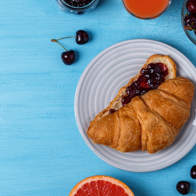 Ontbijt met croissant, jam, fruit en sap.