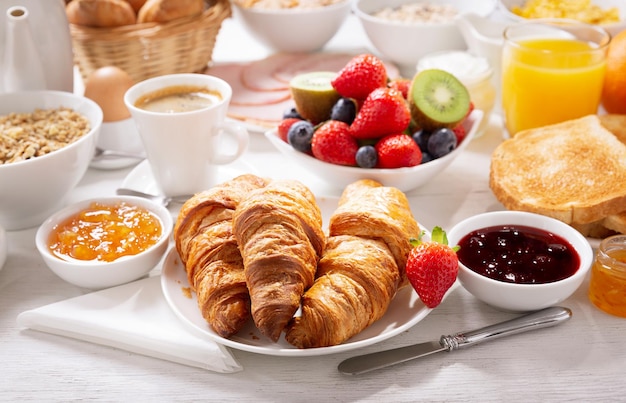 Ontbijt met croissants, koffie, sap, jam, ontbijtgranen en vers fruit