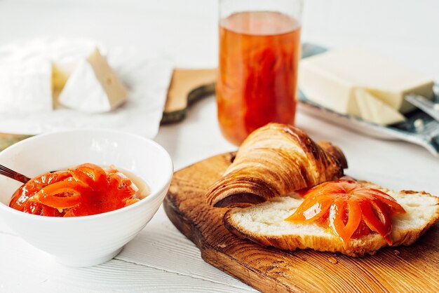 Ontbijt met een verse croissant en een kopje aromatische koffie latte, mandarijnjam, boter en brie. Fruit snijwerk. Gezond ontbijt.