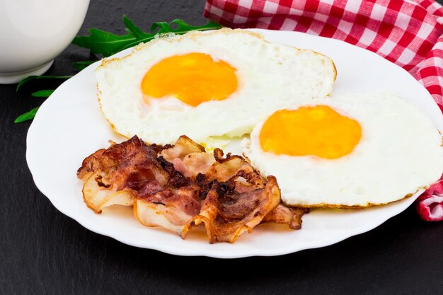 Ontbijt met gebakken eieren en spek op donkere stenen achtergrond.