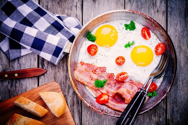 Ontbijt met gebakken eieren, spek, tomaten en peterselie op rustieke tafel