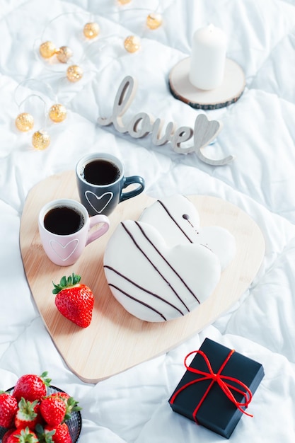 Ontbijt met hartvormige donuts, koekjes, aardbeien en twee kopjes koffie op het dienblad.