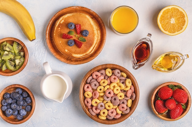 Ontbijt met kleurrijke ontbijtgranenringen, pannenkoeken, fruit, melk, sap