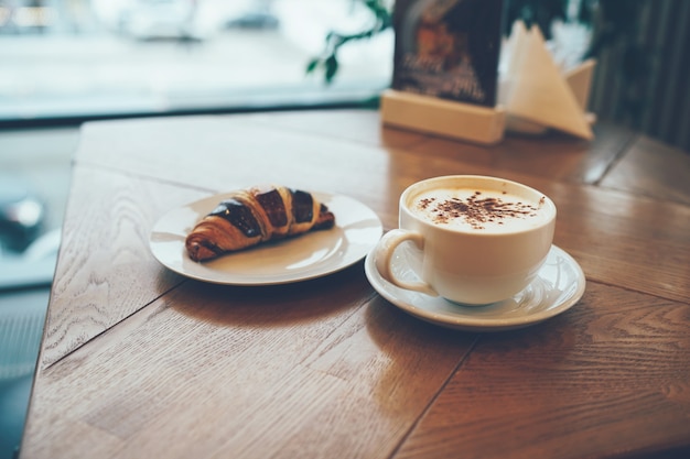 Ontbijt met koffie en een croissant op de tafel bij het raam