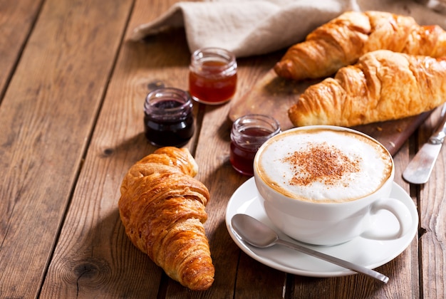 Ontbijt met kopje cappuccino koffie met croissants op houten tafel