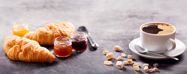 Ontbijt met kopje koffie, croissant en fruitjam op donkere tafel