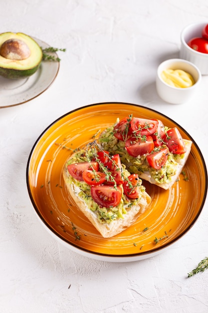 Ontbijt met vegetarische sandwiches met avocado en tomaten op een groot oranje bord