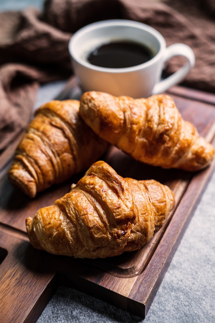 Foto ontbijt met verse croissants en kopje zwarte koffie op een houten bord