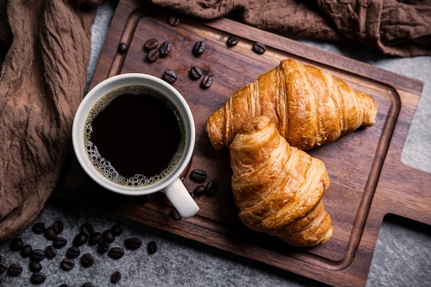 Ontbijt met verse croissants en kopje zwarte koffie op een houten bord