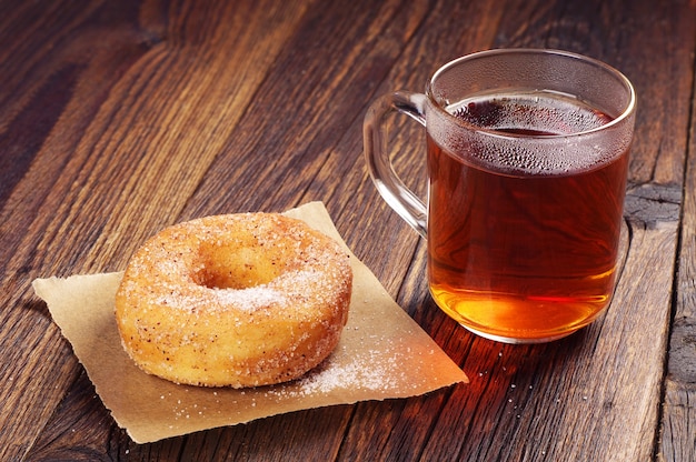 Ontbijt met zoete donut en kopje hete thee op houten tafel