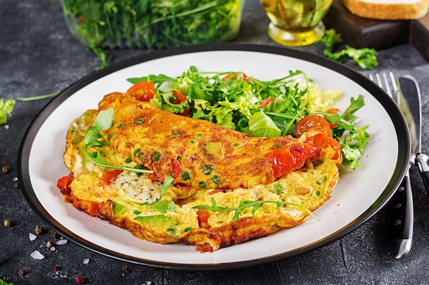 Ontbijt. Omelet met tomaten, avocado, schimmelkaas en groene erwten op witte plaat.