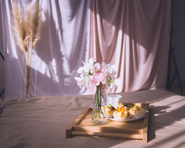 Ontbijt op bed met koffiebroodjes bloemen op houten dienblad in hotelbed of thuis Raamlicht