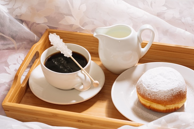 Ontbijt op bed met vers gezette koffie kristalsuiker melk en donut in poedersuiker