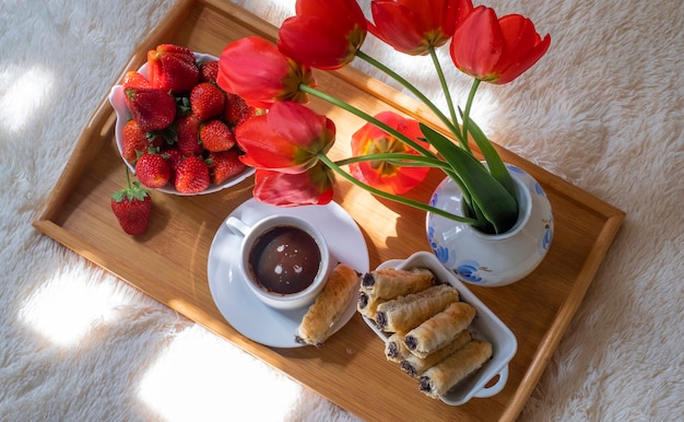 Ontbijt op bed op een dienblad met koffie, koekjes, aardbeien en rode tulpen