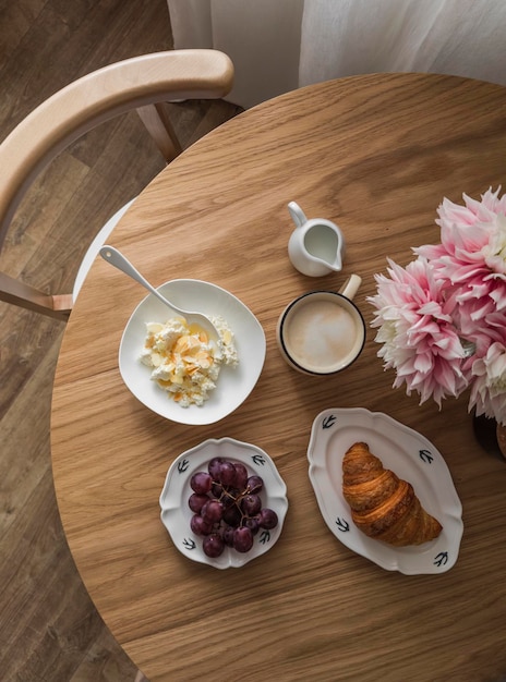 Ontbijt op een houten ronde tafel kwark met honing en amandelbloemblaadjes croissant druiven cappuccino Top uitzicht
