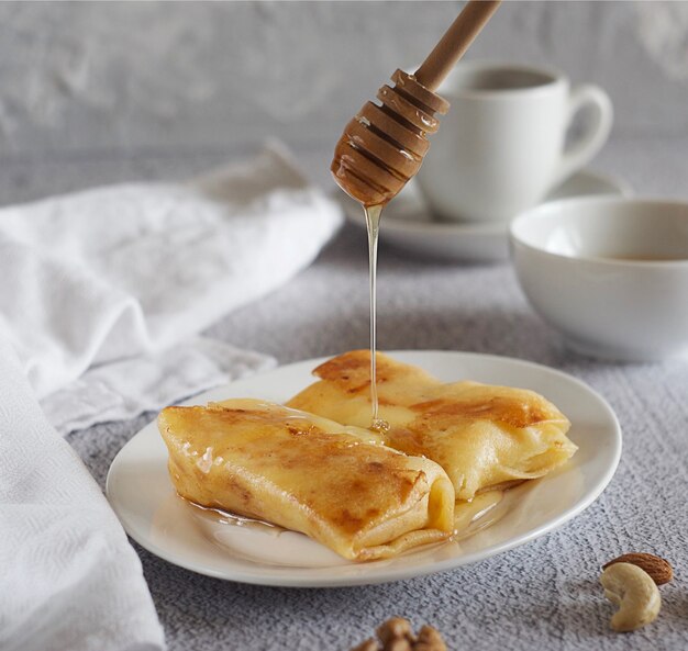 Ontbijt. Pannenkoeken met honing op een bord, ernaast is een handdoek. Achter een kom honing en een mok koffie.