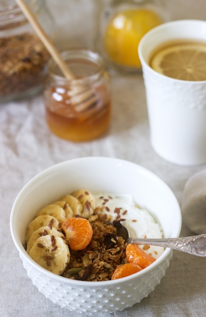 Ontbijt van muesli met yoghurt en thee en forsythia bloemen op een linnen tafellaken. Rustieke stijl.