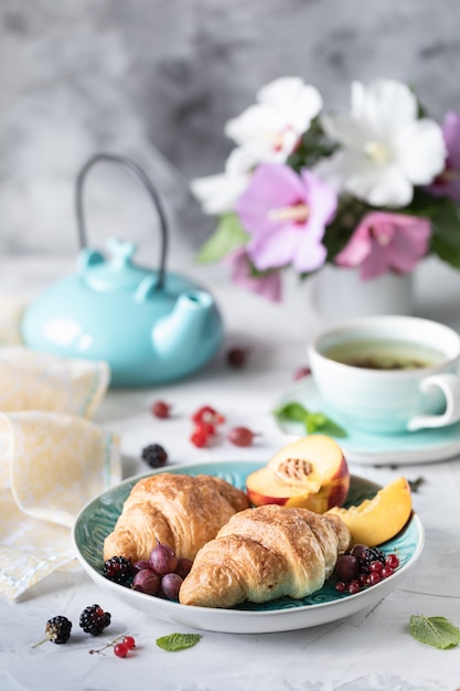 Ontbijt van verse bessen en fruit met croissants, thee een boeket van zomerbloemen.