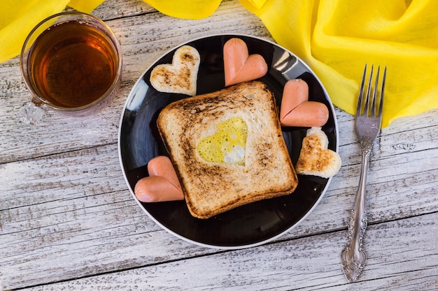 Ontbijt voor de viering van Valentijnsdag - toast met roerei in de vorm van hartjes, worstjes en thee