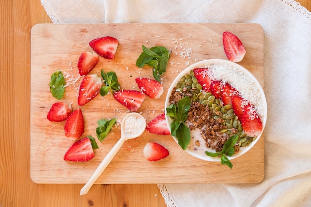 Ontbijtbessen smoothie bowl gegarneerd met aardbei pompoenpitten, kokos muesli en verse munt