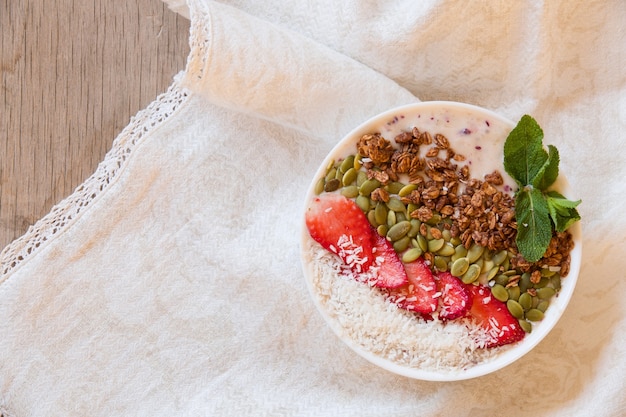 Ontbijtbessen smoothie bowl gegarneerd met aardbei pompoenpitten, kokos muesli en verse munt