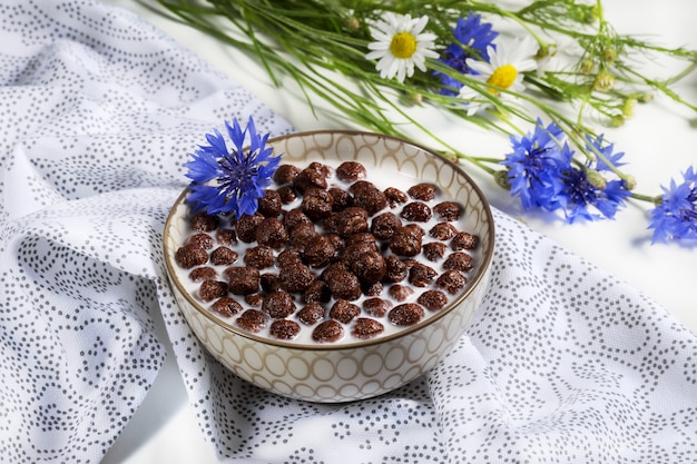 Ontbijtgranen, Chocoladegranen in melk met korenbloembloem op een natuurlijk servet, concept gezonde voeding voor kinderen, zachte nadruk.