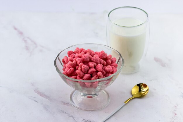 Ontbijtgranen in de vorm van harten een kom en een glas melk op een witte marmeren achtergrond snacks met frambozensmaak