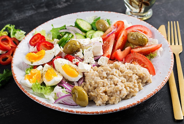 Ontbijthavermoutpap met Griekse salade van tomaten, komkommers, olijven, fetakaas en eieren. Gezonde evenwichtige voeding.