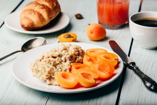 Ontbijtset. pap met gesneden abrikoos, kopje koffie, glas grapefruitsap en croissant