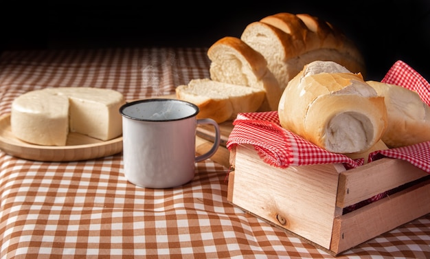 Ontbijttafel in Brazilië met brood, kaas, kopje koffie en accessoires op een bruin en beige geruit tafelkleed.