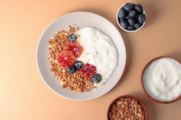 Ontbijttafel met mueslikom met griekse yoghurt versierd met bloedsinaasappels, bosbessen en kokosbeige achtergrondingrediënt voor ontbijt bovenaanzicht