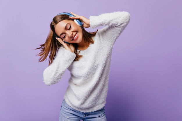 Сontented girl in excellent mood closed her eyes from pleasure of her favorite rhythmic song Shot taken in studio of model posing in white soft sweater