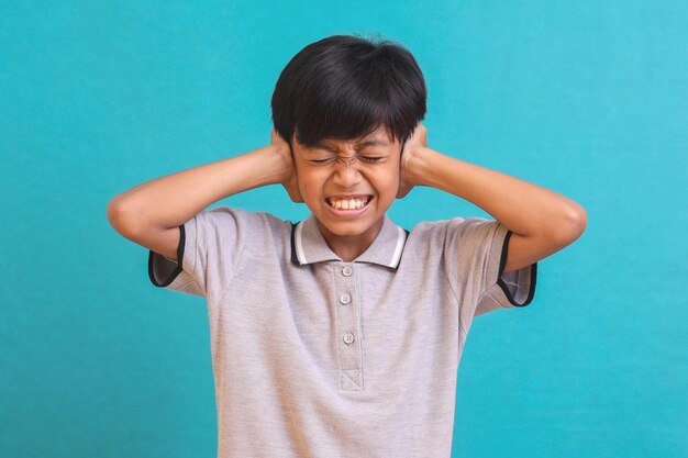 Ontevreden Aziatische jongen die zijn oren bedekt tegen het lawaai geïsoleerd op groene achtergrond